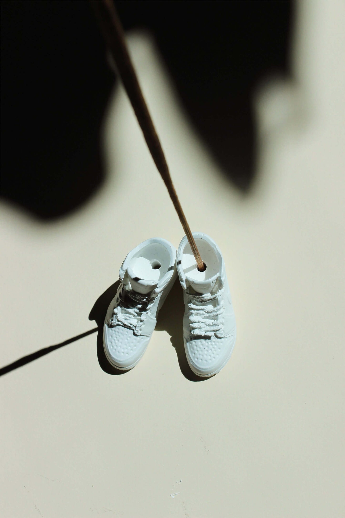 White sneakers hanging by a thin rope on a light background - incense holder