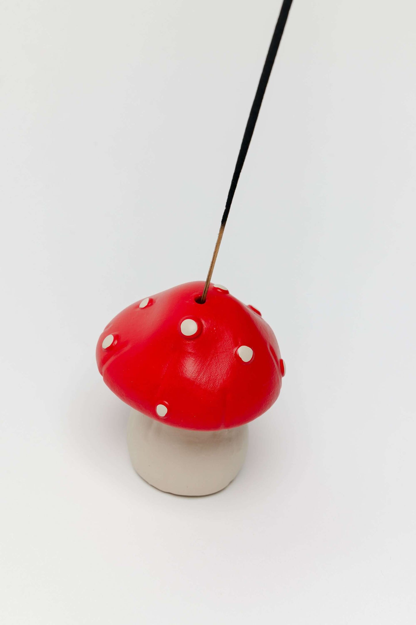 Mushroom-shaped incense holder with a red cap and white spots on a white background