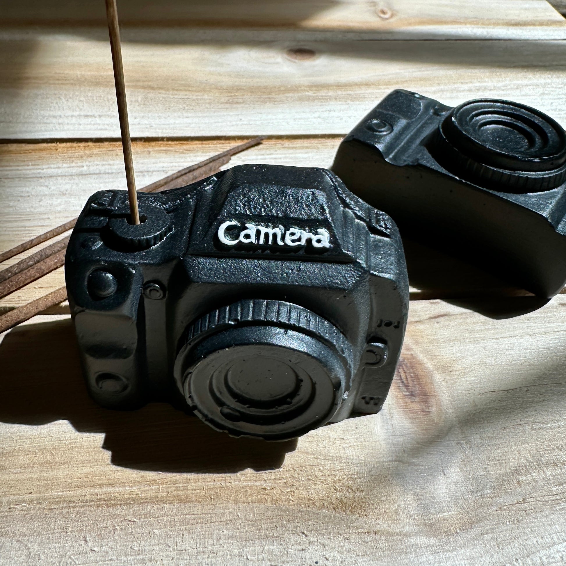 Two black camera incense holders facing forward and side on a wooden table