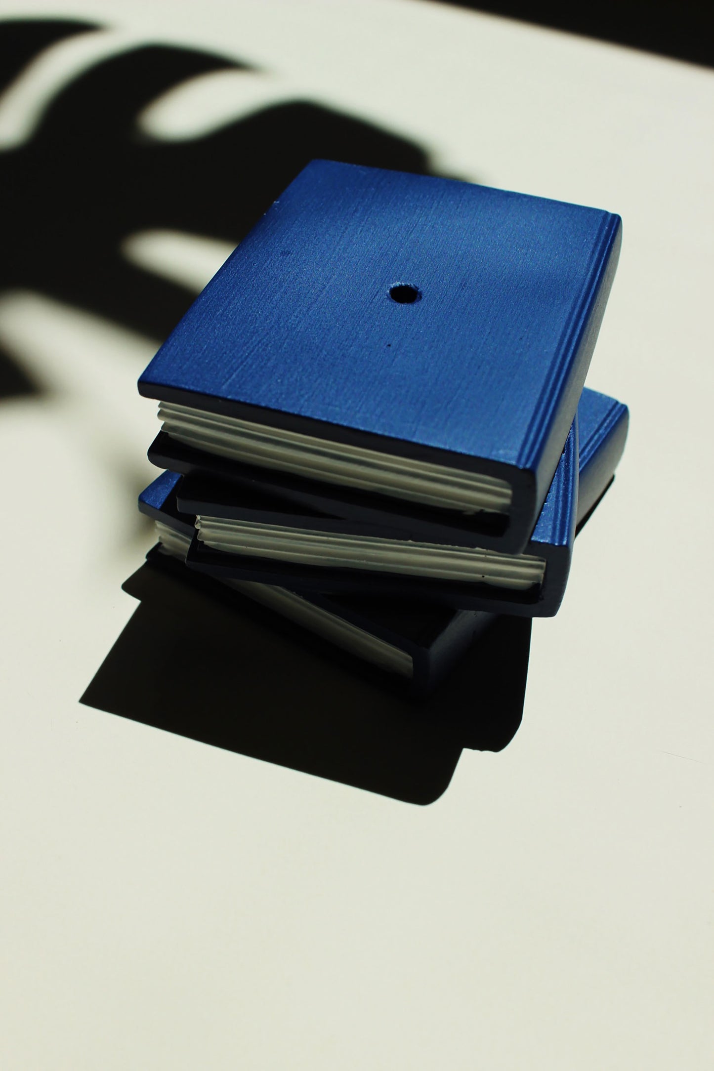 Stack of blue and black books on a light surface with shadows. Incense burner