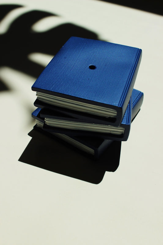 Stack of blue and black books on a light surface with shadows. Incense burner