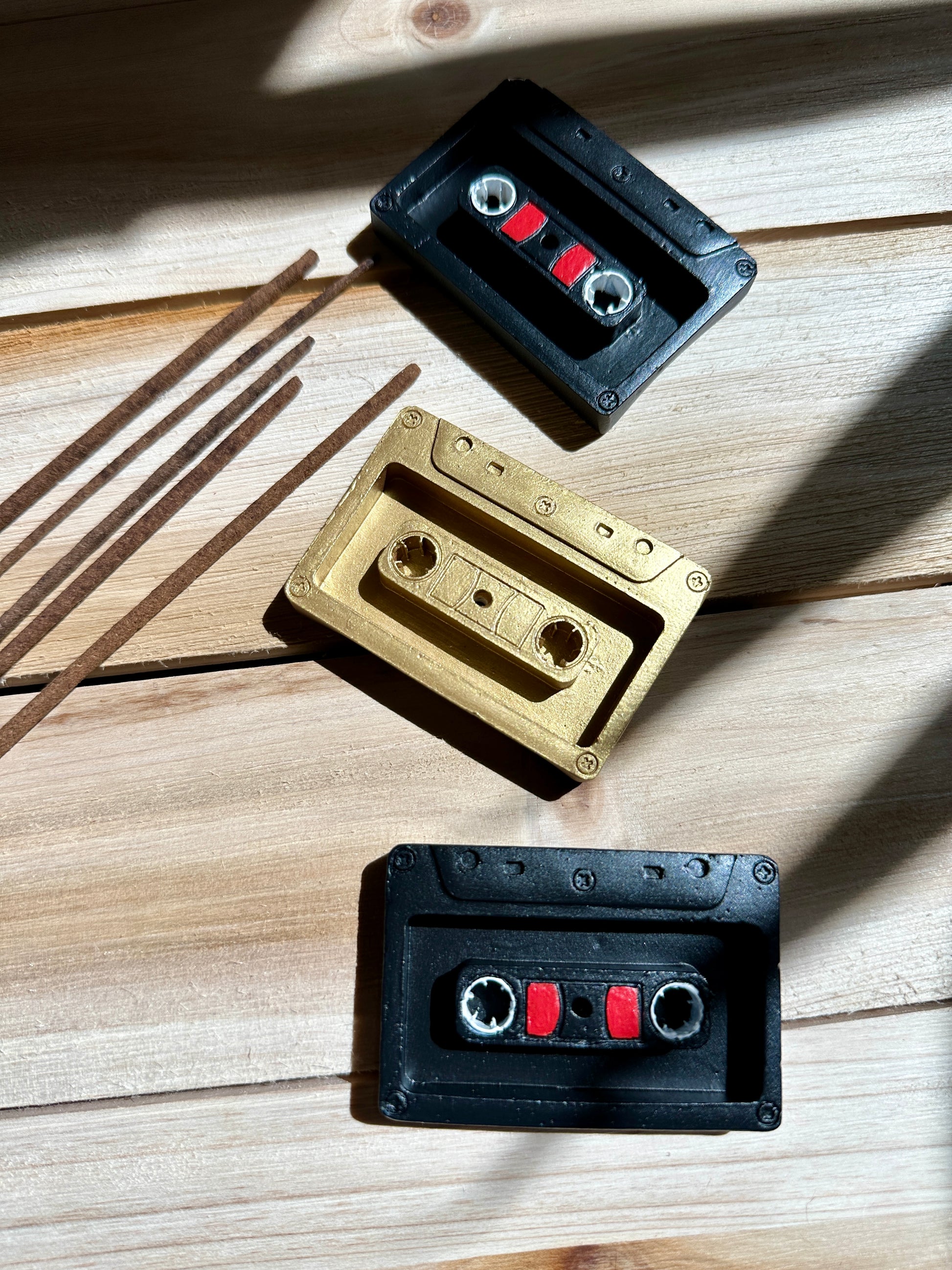 Ceramic resin cassette tape incense stick holders in black and gold on a wooden surface with incense sticks