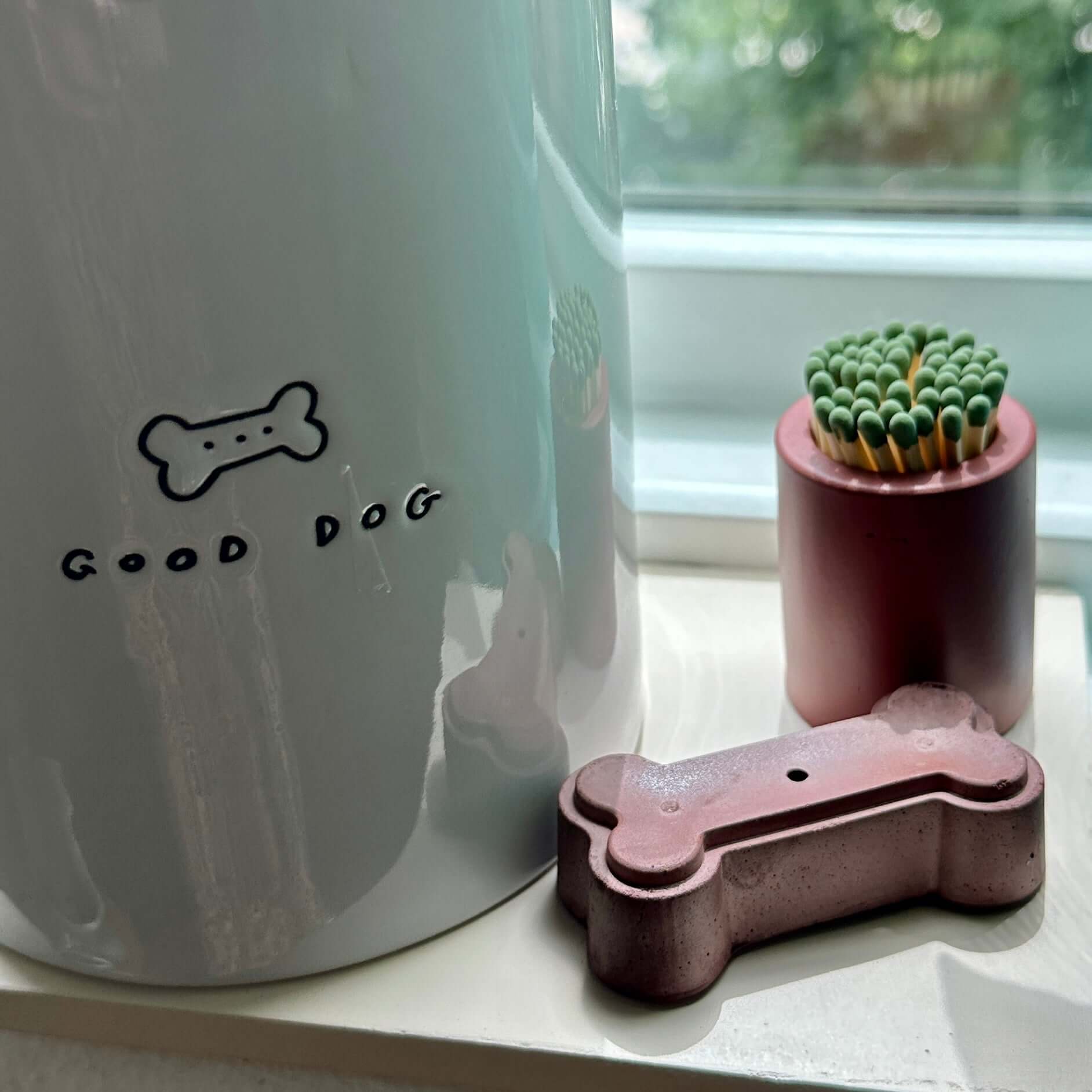 Give a Dog a Bone Incense Stick Holder in burgundy brown placed near a white "Good Dog" container and a small cactus on a windowsill.