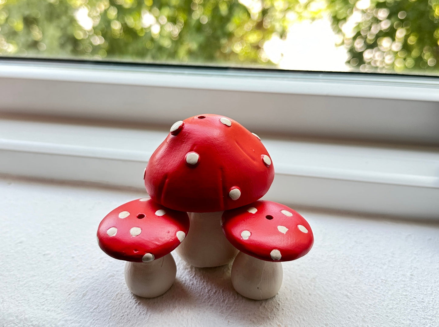 Ceramic resin mushroom incense holder by window with green foliage background.