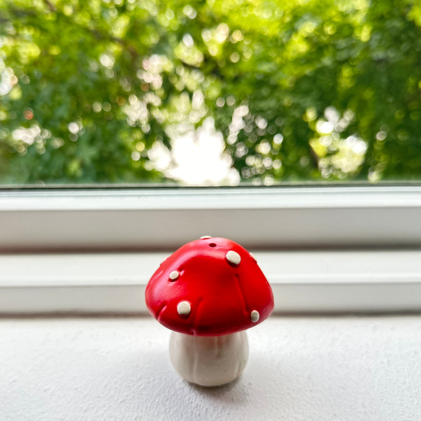 Ceramic resin red mushroom incense holder by window.