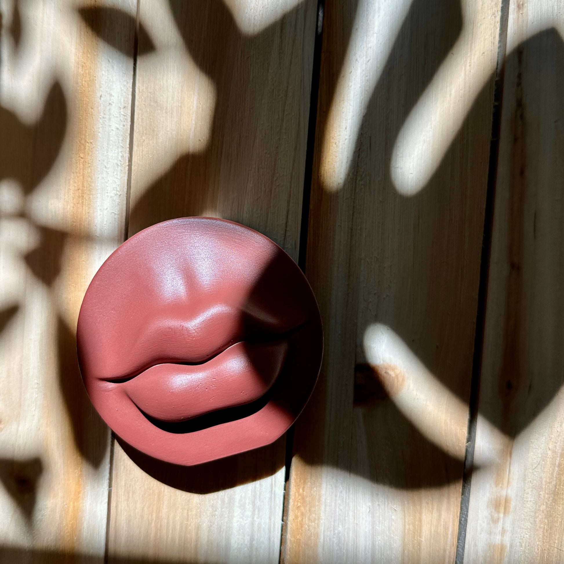 Lip shape incense holder made of ceramic resin against a wooden background with shadows and light play.