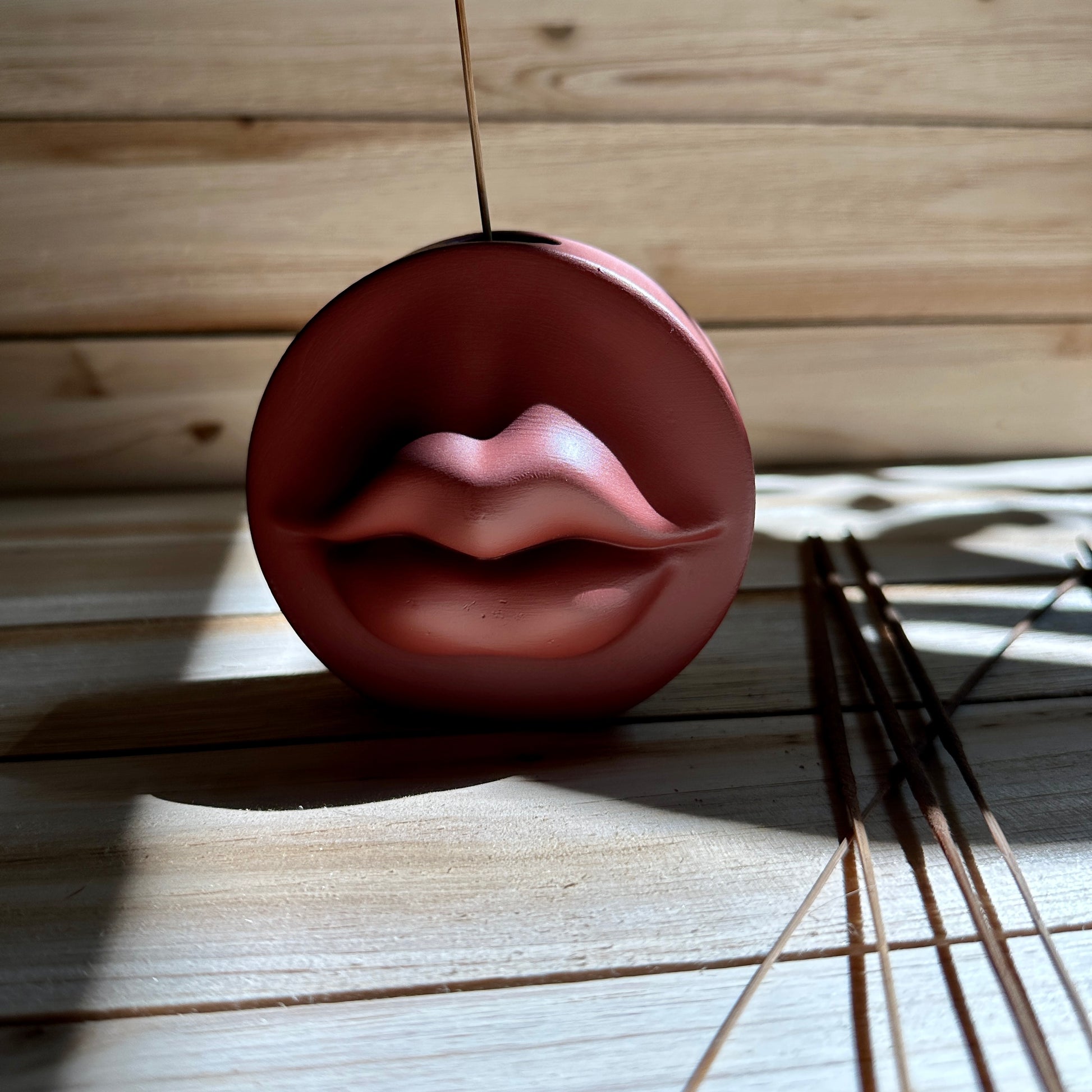 Lip-shaped ceramic resin incense holder on a wooden surface with incense sticks nearby