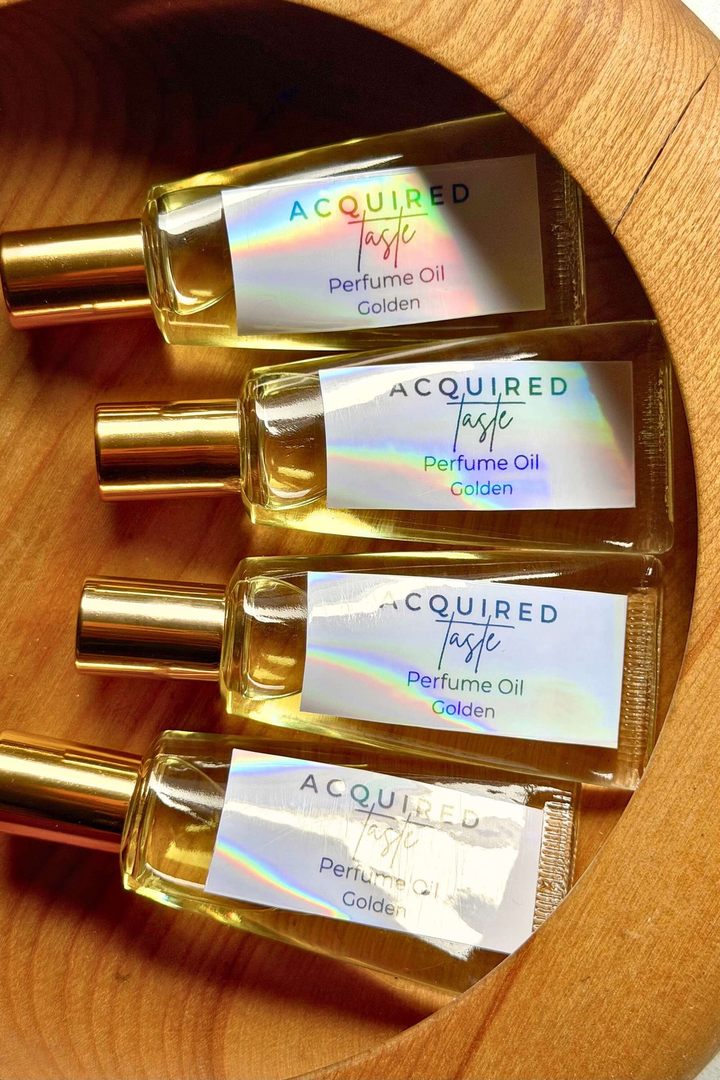 Four bottles of Acquired Taste perfume oil on a wooden surface