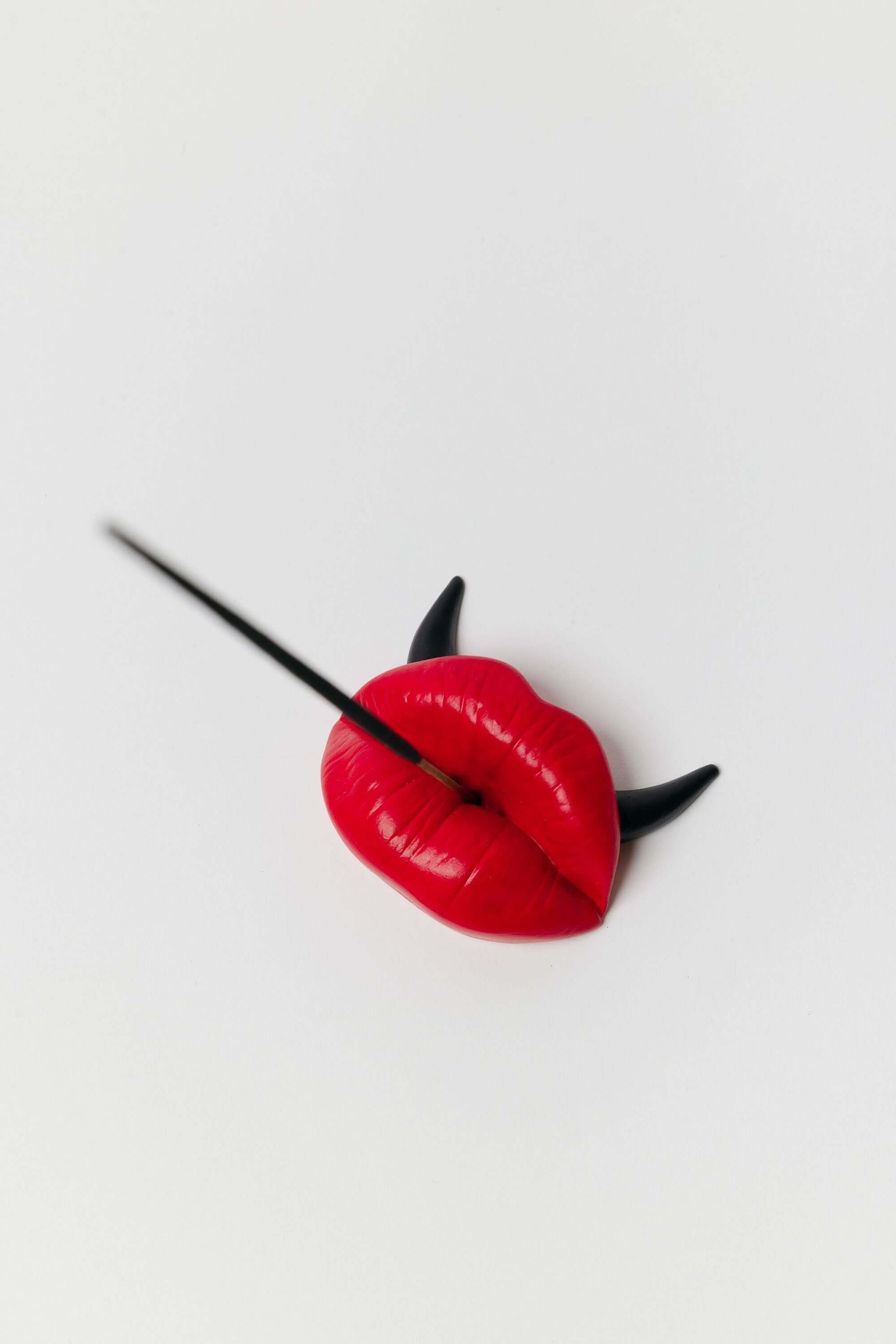Red lip-shaped hairpin with black horns on a white background