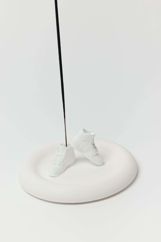 White ceramic shoes on a white pedestal with a black rod against a white background