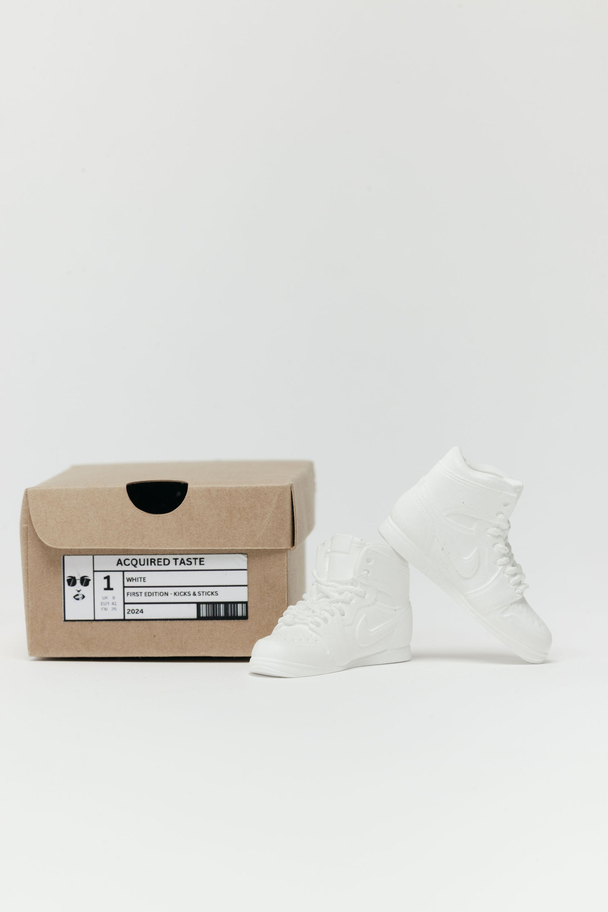 White high-top sneakers next to a brown box with a label on a white background - incense holder