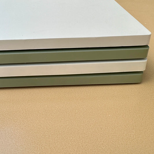 Stack of white and sage green flat ceramic incense trays on a beige surface